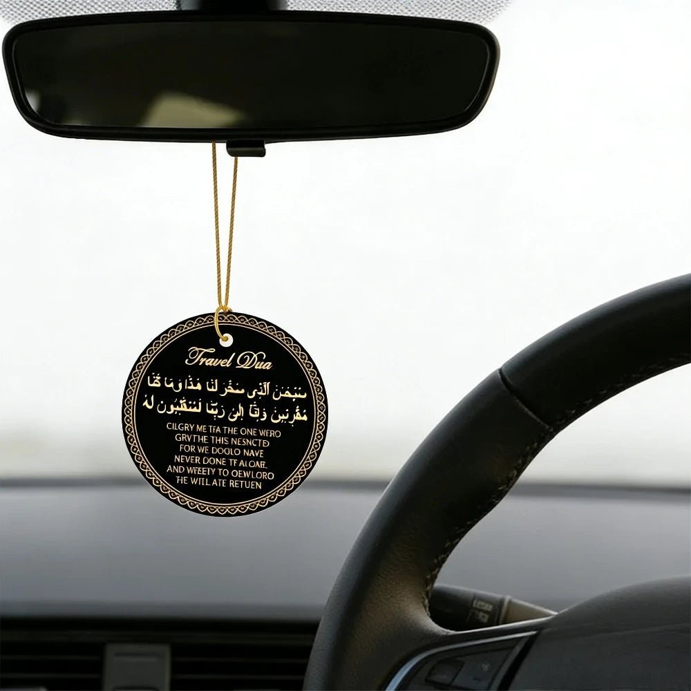 A round gold prayer tag with Arabic and English text hangs from a black light fixture above a car steering wheel.