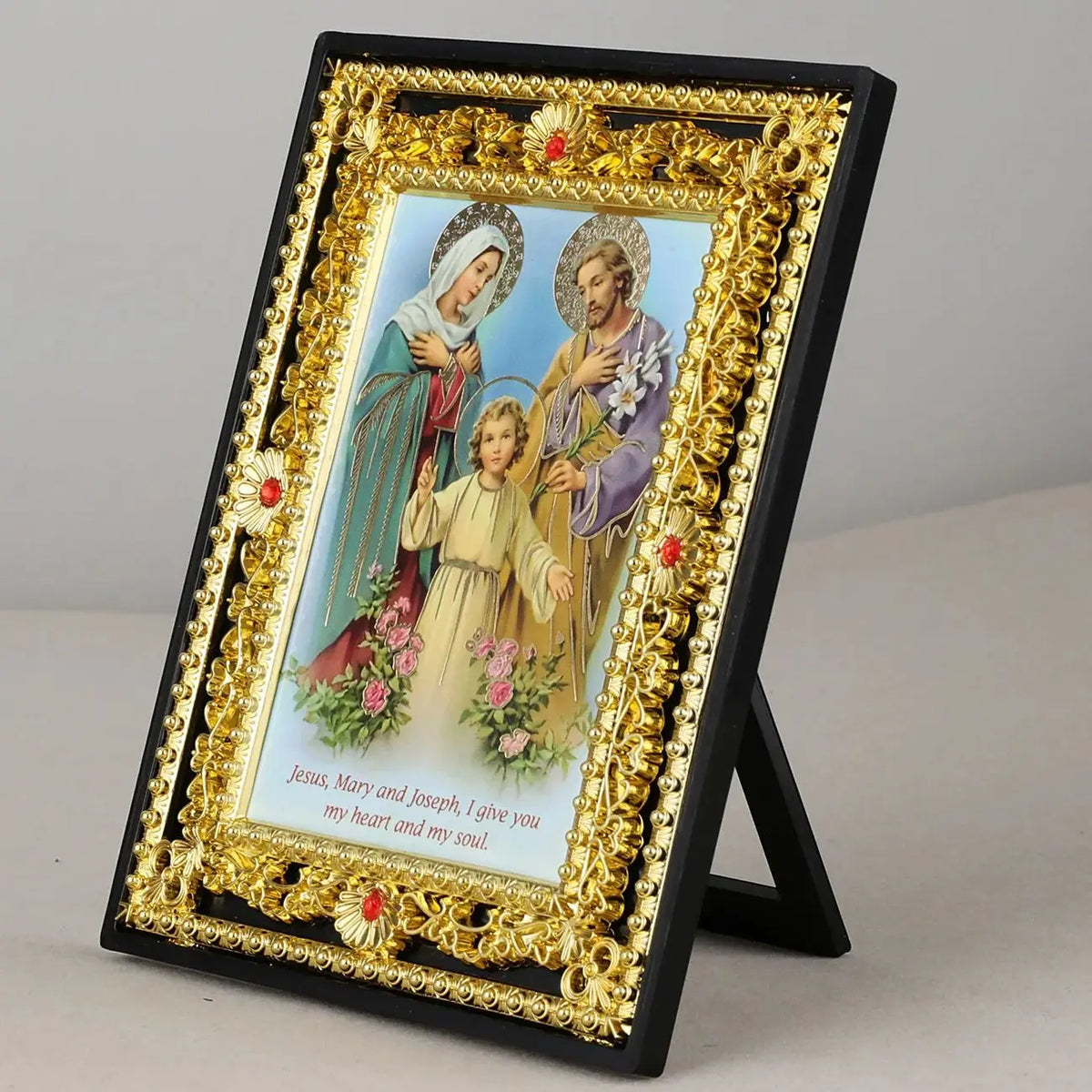 A framed Catholic Holy Family icon featuring Jesus, Mary, Joseph, and an archangel, displayed in a black and gold ornate fram