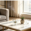 A tall, slender glass incense burner with a gourd shape and ash catcher emitting smoke on a white marble table.