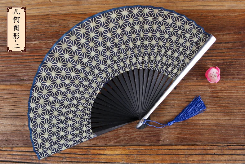 A folding hand fan with a dark patterned silk cover and a silver frame resting on a wooden surface.