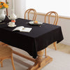 A black rectangular tablecloth is set on a wooden dining table with white porcelain and floral decorations.