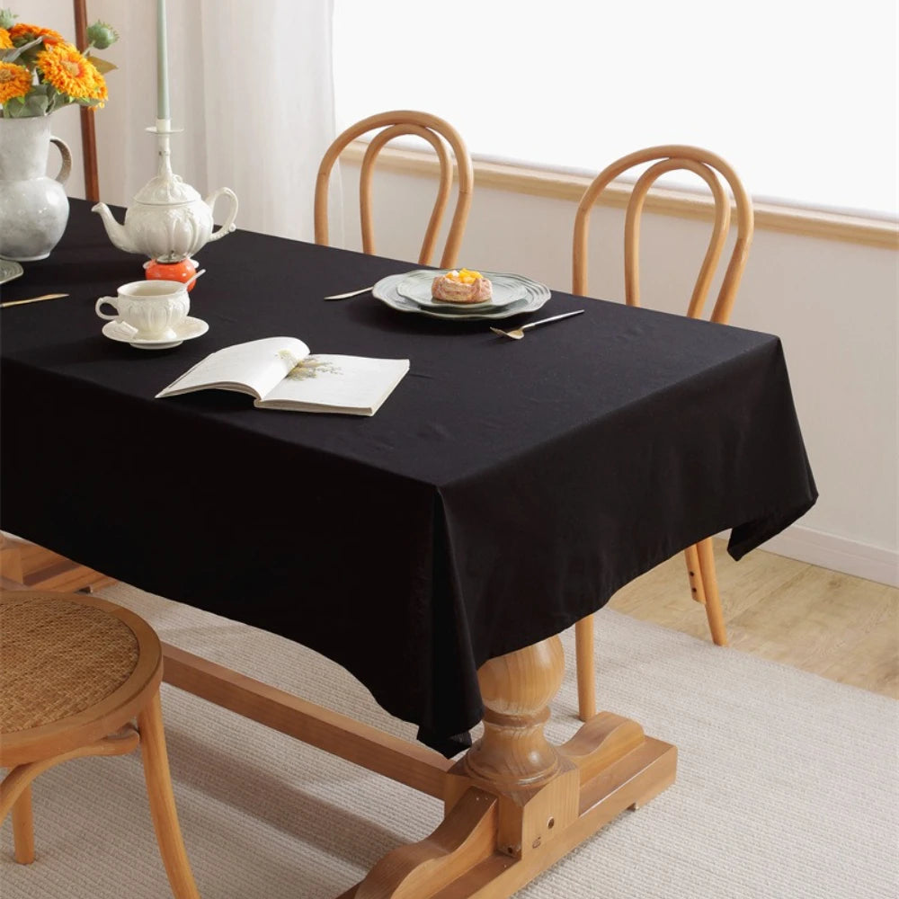 A black rectangular tablecloth is set on a wooden dining table with white porcelain and floral decorations.