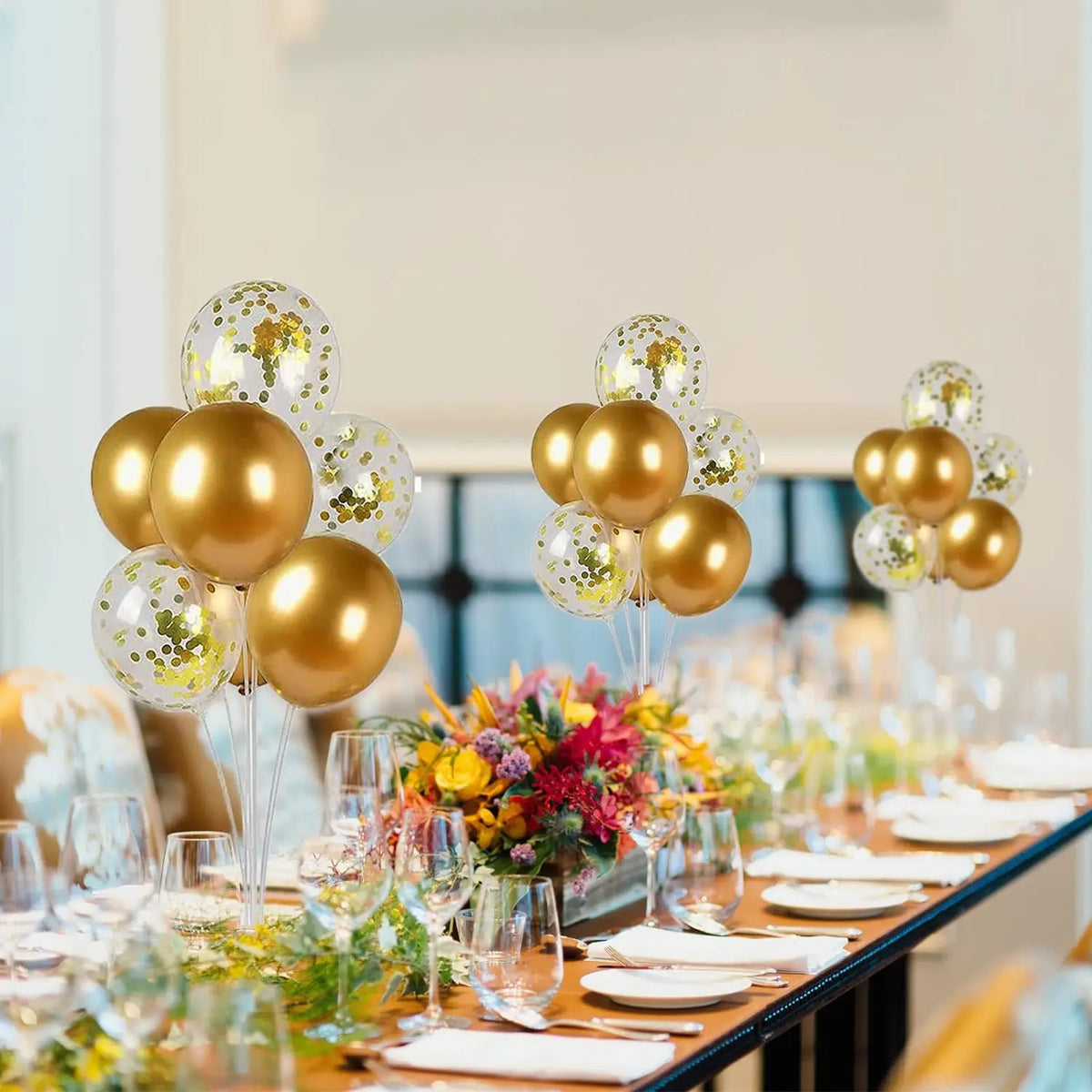 A table setting featuring gold and white balloons and floral arrangements for an event.