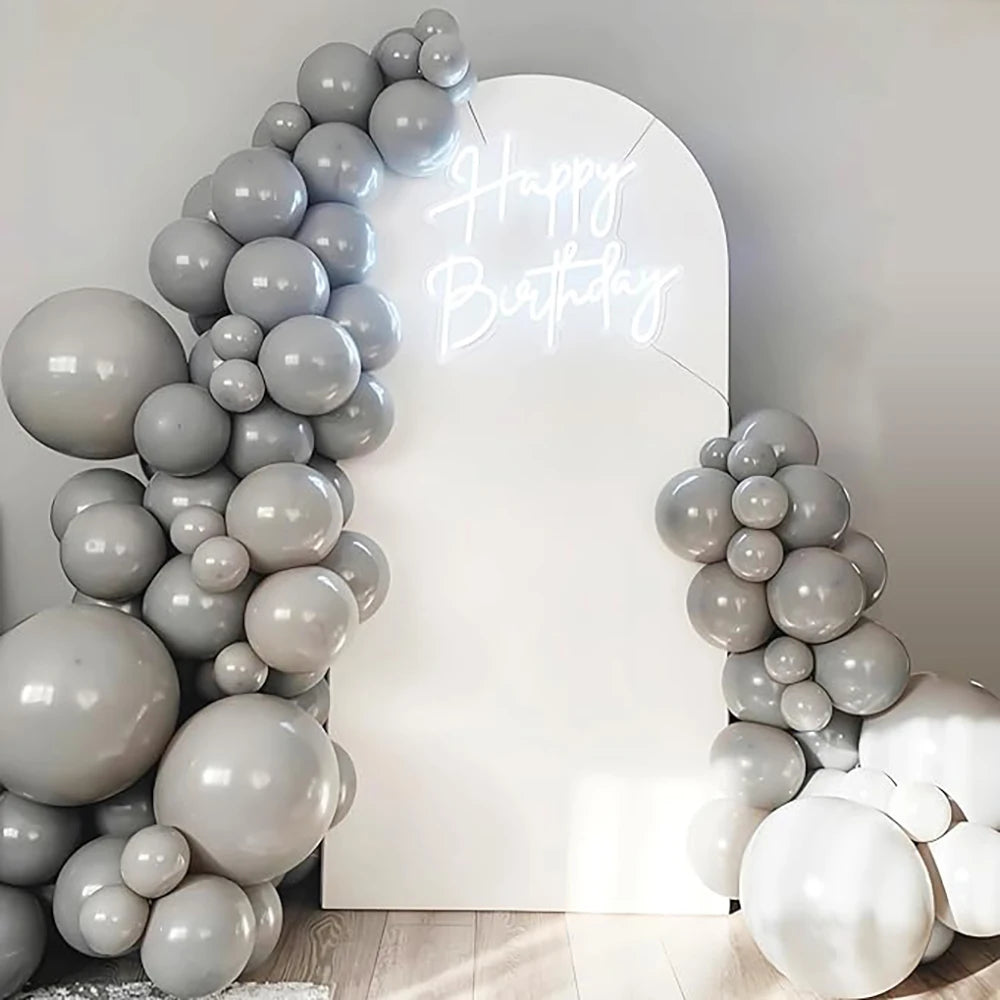 A display of round gray and white latex balloons forming a balloon arch with 'Happy Birthday' written in light glow.