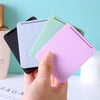 A hand holds a compact foldable travel makeup mirror with multiple colored cases, showing the product's design.