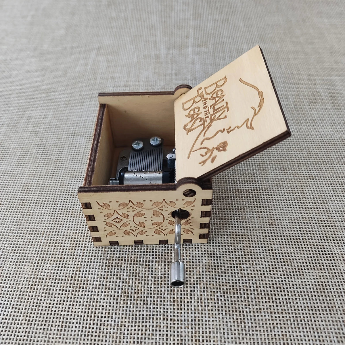 An antique carved wooden music box with a hinged lid showing a handwritten inscription and a metal cylinder.