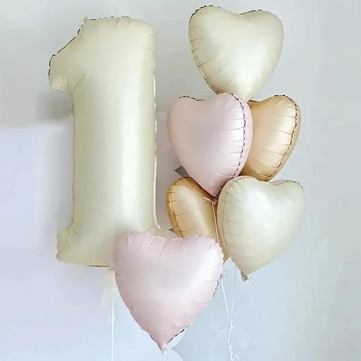 A cluster of light pink and cream heart-shaped foil balloons floating against a white background.