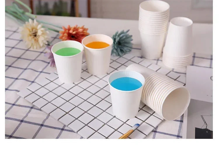 A collection of white disposable paper cups filled with various colored drinks on a checkered napkin.