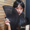 A close-up of a woman holding a black hand carved bamboo folding fan against a tiled wall.