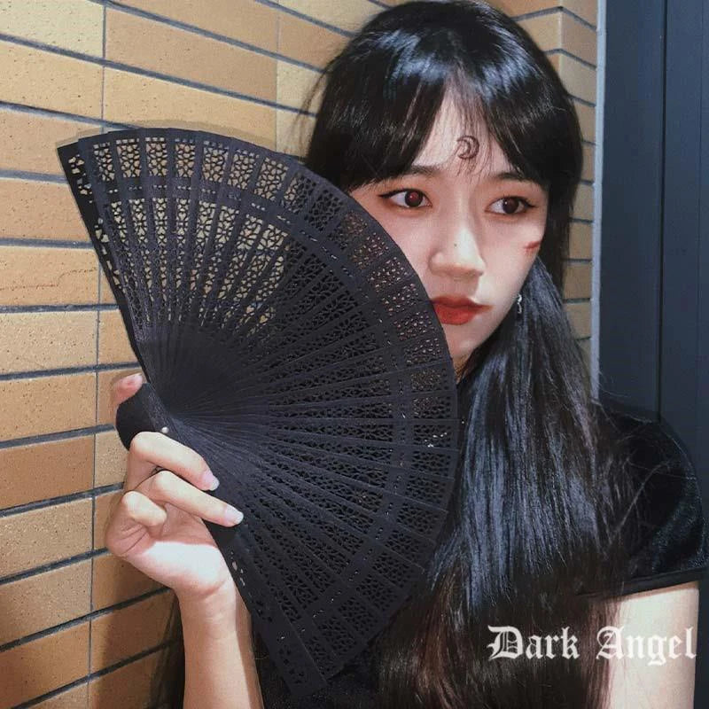 A close-up of a woman holding a black hand carved bamboo folding fan against a tiled wall.