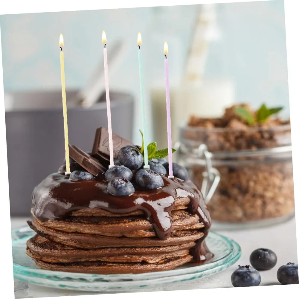 A stack of brown pancakes topped with blueberries and chocolate drizzle, surrounded by thin candles.