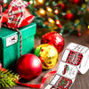 A roll of Christmas present stickers with festive designs and a red ribbon, set against a blurred background of holiday light