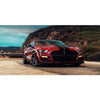 A red Ford Mustang Shelby GT parked on a dirt road with mountains in the background.