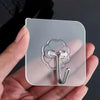 A hand holds a transparent self-adhesive wall hook with a metal hook and multiple small hooks.