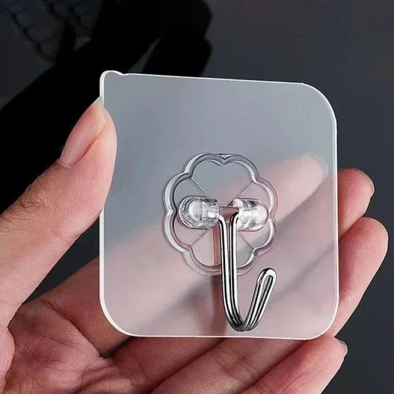 A hand holds a transparent self-adhesive wall hook with a metal hook and multiple small hooks.
