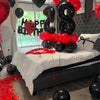 A red and black balloon garland decoration set featuring foil number balloons strung across a bedroom setting.