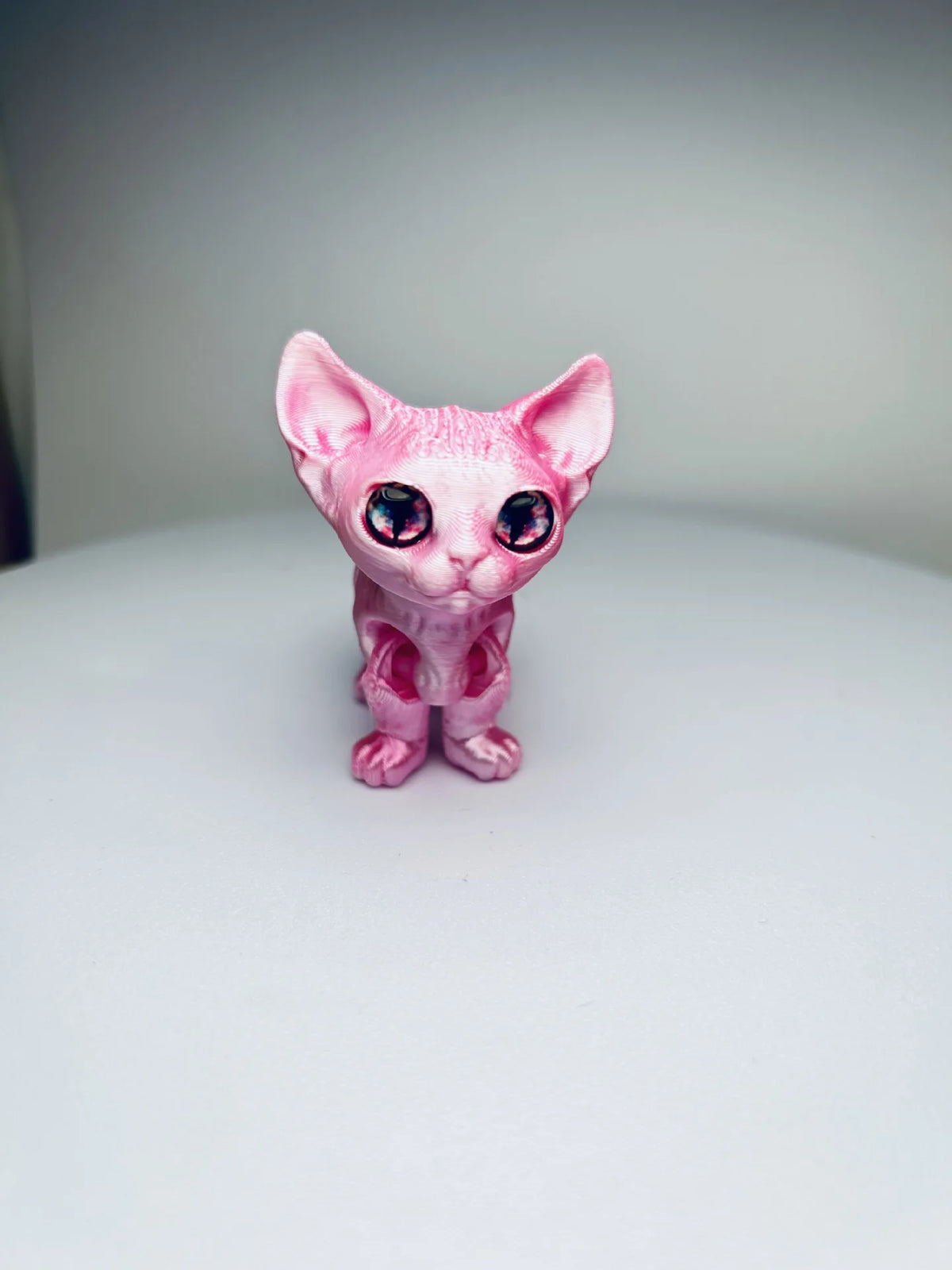 A pink articulated 3D printed figurine of a Siamese cat with large blue eyes.