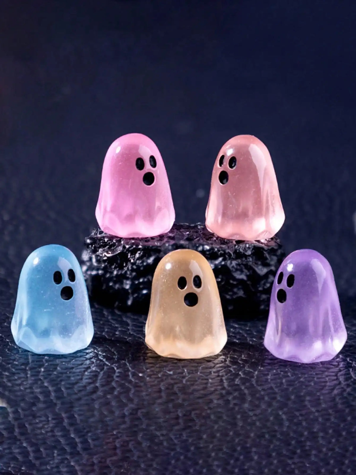 A collection of luminous ghost mini figurines in pink, purple, blue, and yellow resting on a dark surface.