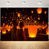 A couple stands in a dark field surrounded by numerous glowing orange lanterns at night.