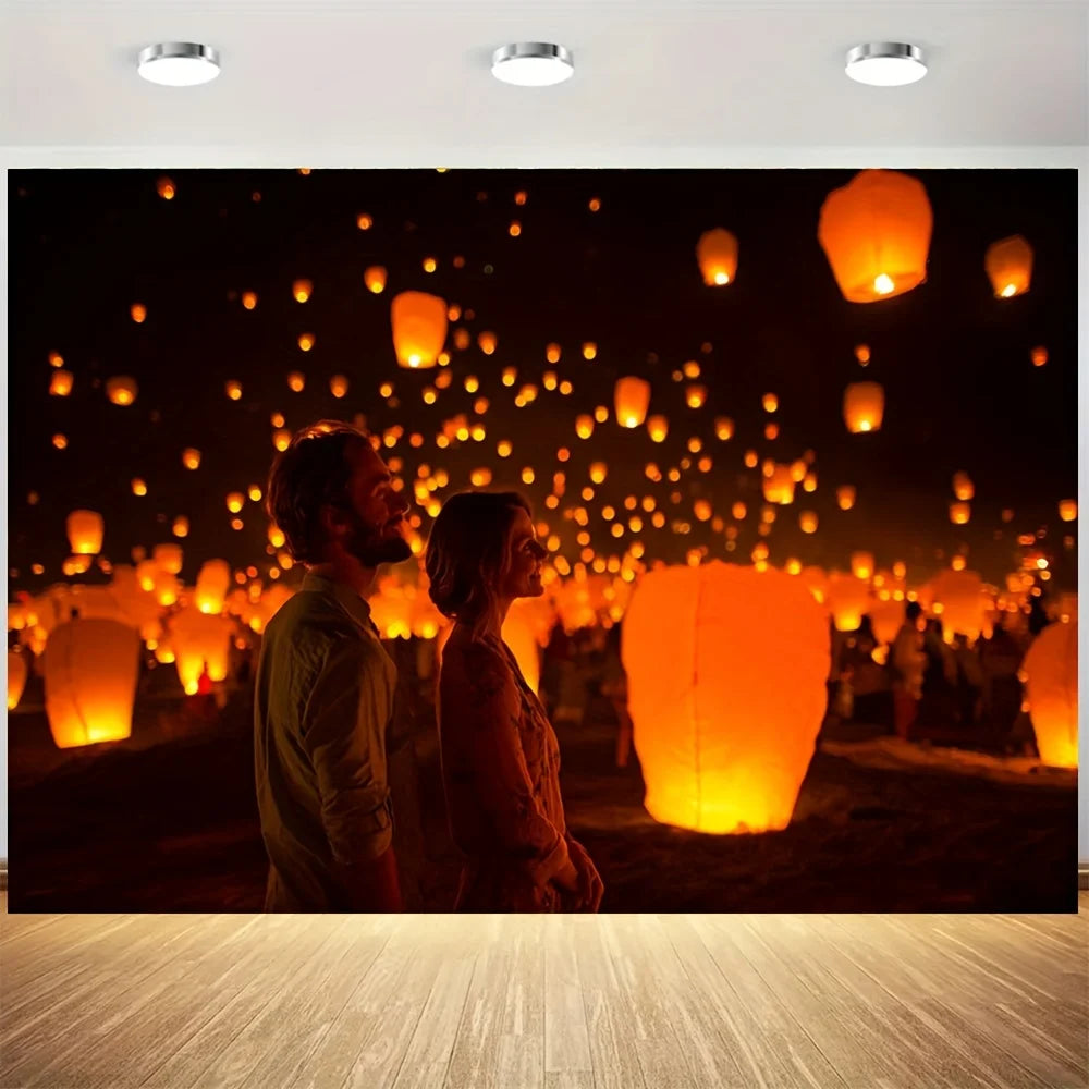 A couple stands in a dark field surrounded by numerous glowing orange lanterns at night.