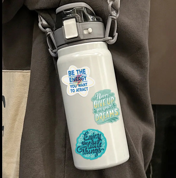 A white water bottle with a gray cap and inspirational quotes printed on the body, hanging from a gray strap.