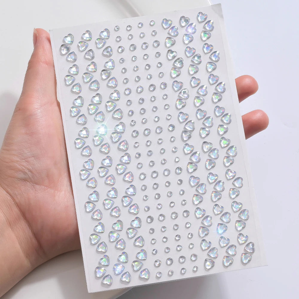 A hand holds a sheet of glitter gem stick-on facial tattoos featuring various heart and diamond shapes.