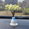 A small black tree branch with white flowers is mounted on a blue and white ceramic ornament for a car dashboard.