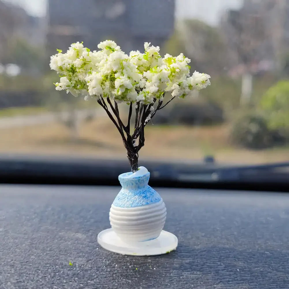A small black tree branch with white flowers is mounted on a blue and white ceramic ornament for a car dashboard.