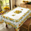A yellow sunflower printed tablecloth displayed on a wooden table in a bright dining room setting.