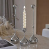A set of three silver waterdrop design candle holders with white candles displayed on a table.