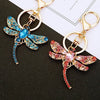A crystal dragonfly keychain featuring blue and pink iridescent wings and a gold-toned carabiner clip.