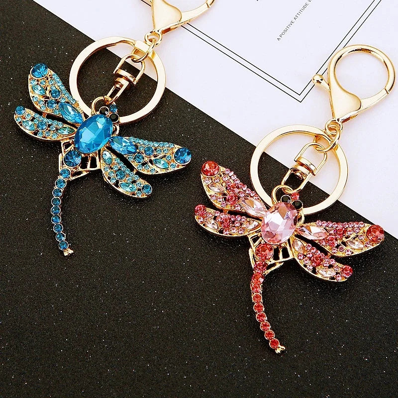 A crystal dragonfly keychain featuring blue and pink iridescent wings and a gold-toned carabiner clip.
