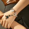 A hand wearing a silver ring and a letter charm with butterfly stickers on the wrist against a dark background.