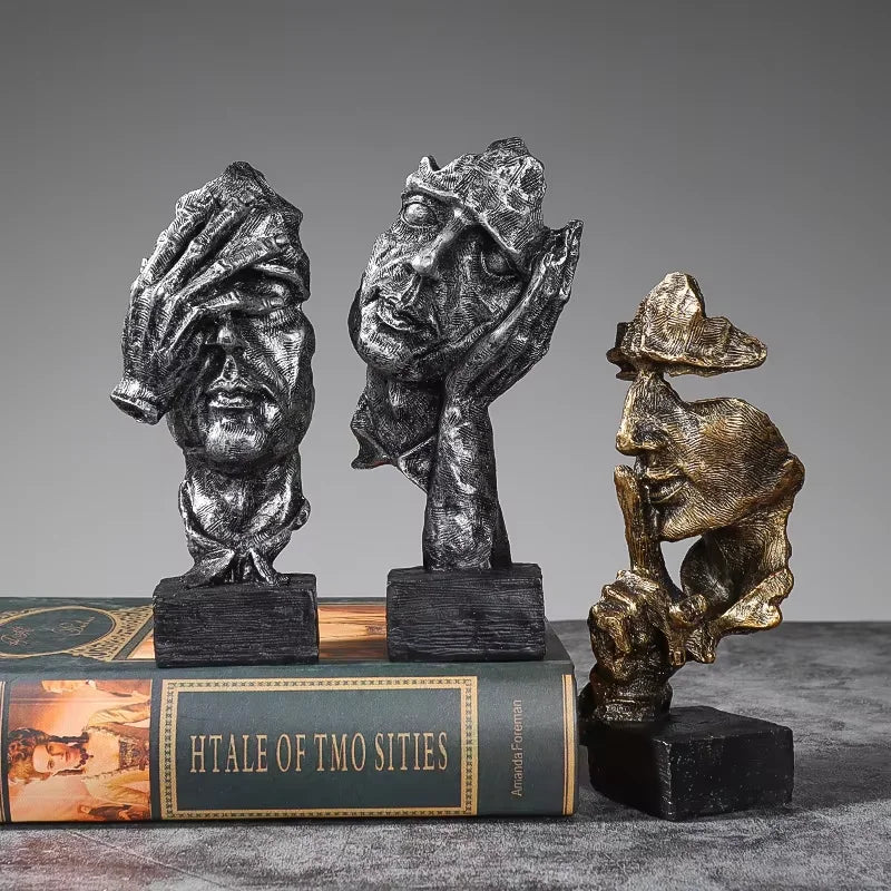 A set of three resin figurines depicting faces in a dark, textured finish displayed on an open book.