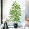 An artificial bamboo branch with bright green leaves displayed in a dark pot on a modern table.