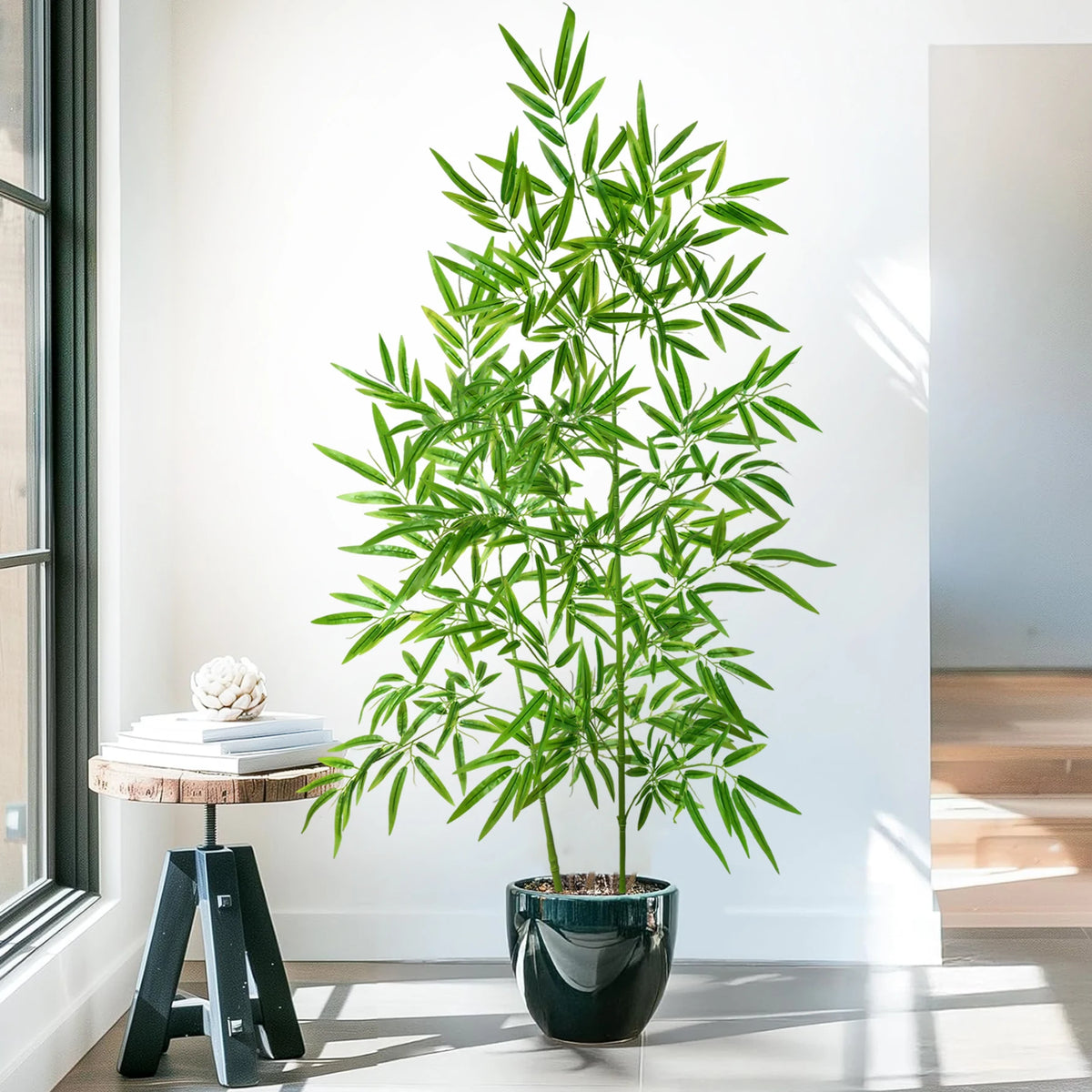 An artificial bamboo branch with bright green leaves displayed in a dark pot on a modern table.