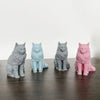 A row of four silicone cat molds in various shades of gray, blue, and pink are displayed on a dark wooden surface.