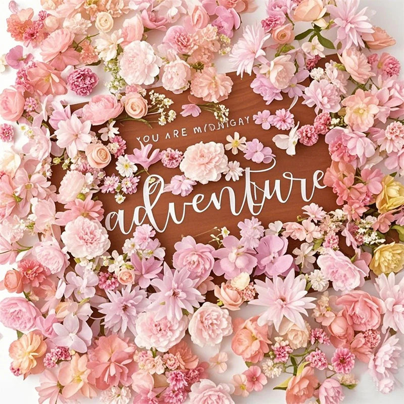 A dense arrangement of pink and peach silk artificial flower heads surrounding a wooden plaque with the word adventure writte