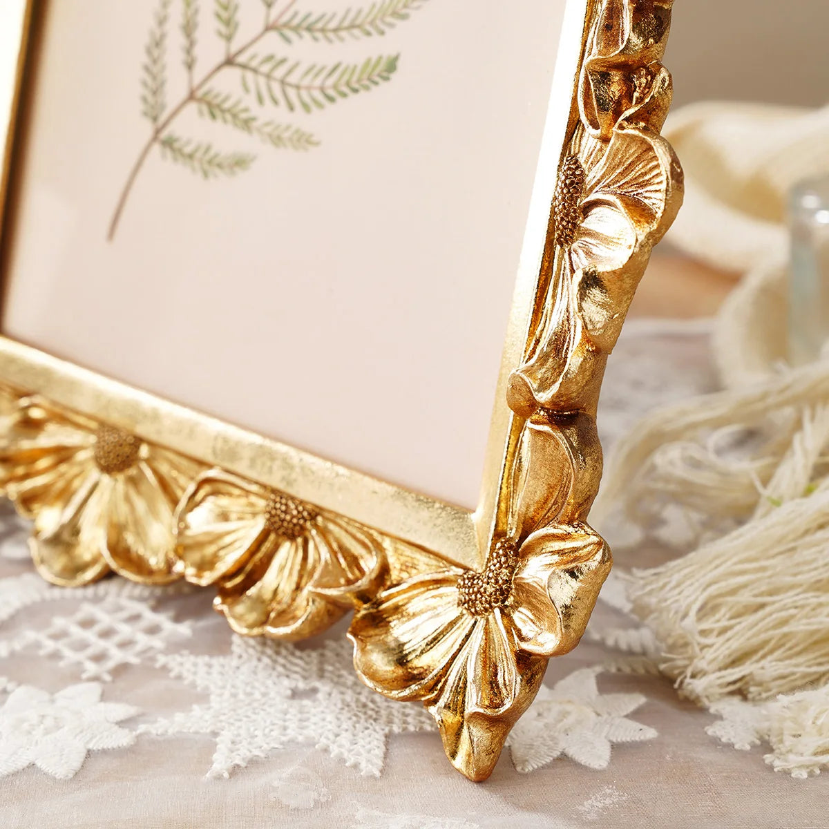A golden 3D resin photo frame with an elegant floral design and greenery displayed on a light surface.