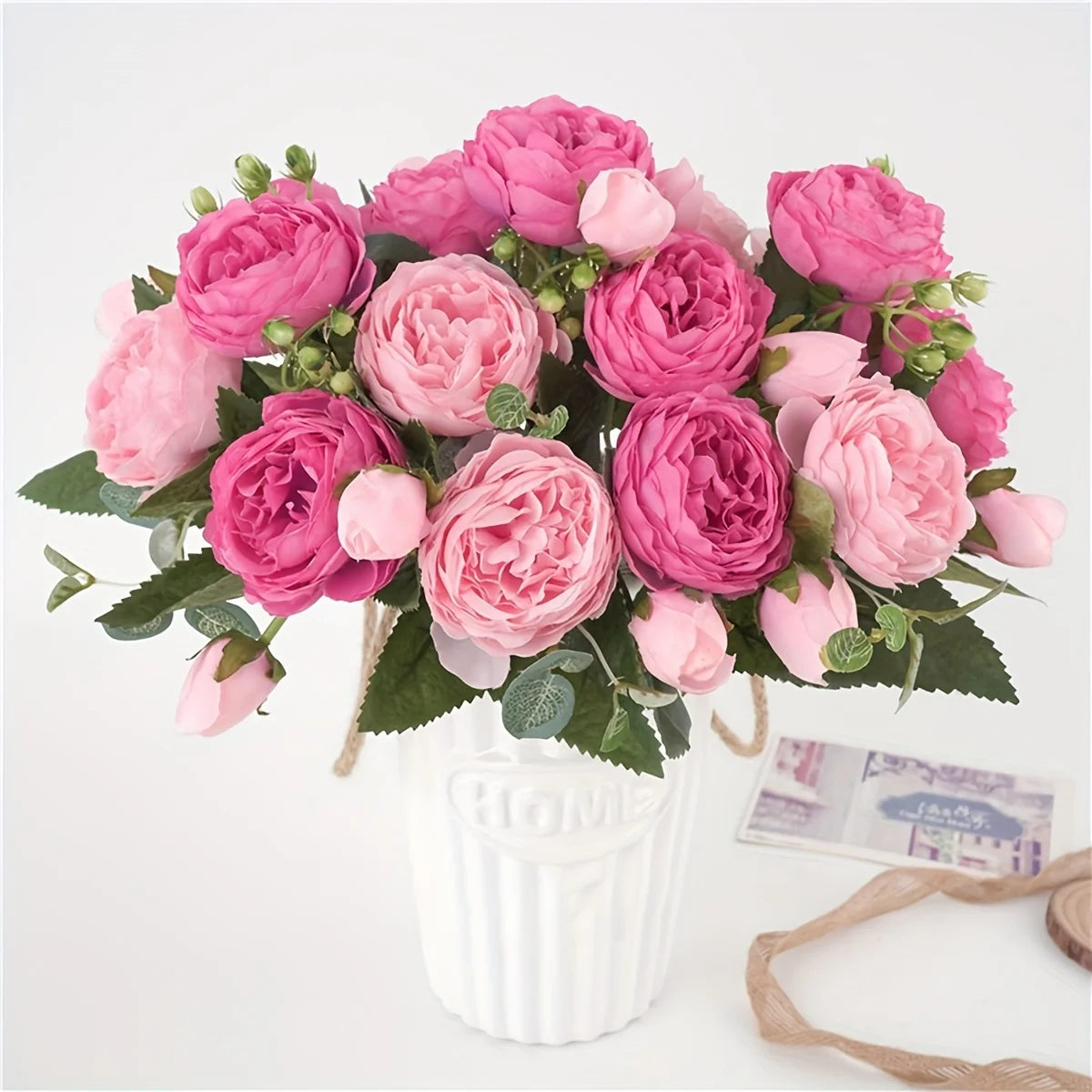 Ein Strauß künstlicher Seerosen- und Pfingstrosen in rosa und magentafarbenen Tönen in einer weißen Vase.