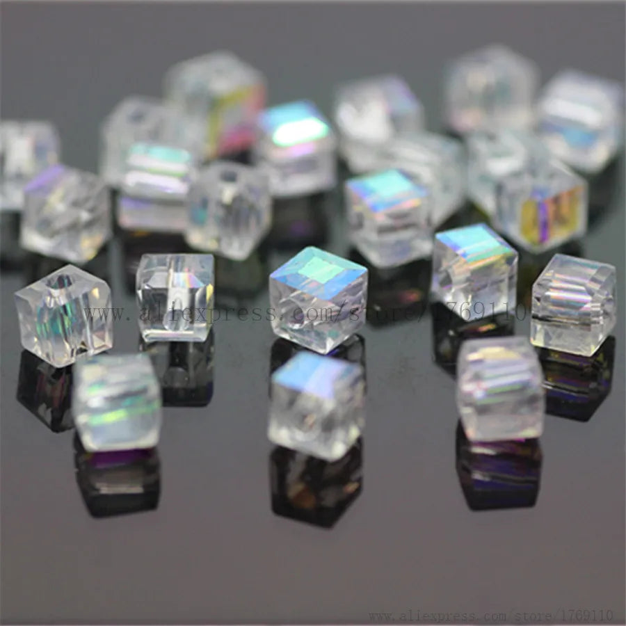 A collection of square cut glass crystals and beads reflecting on a dark surface.