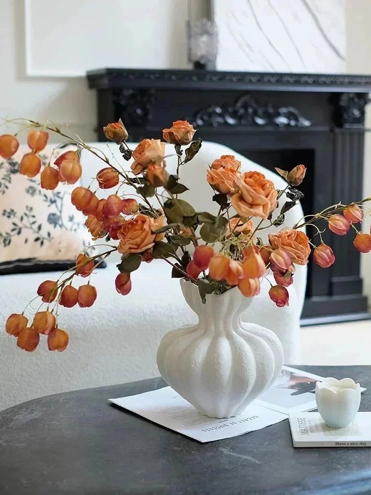 A white ceramic vase filled with dried orange and brown floral elements sits on a dark surface.