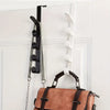 A brown leather handbag is hanging on a white door with black and white over-the-door hooks.