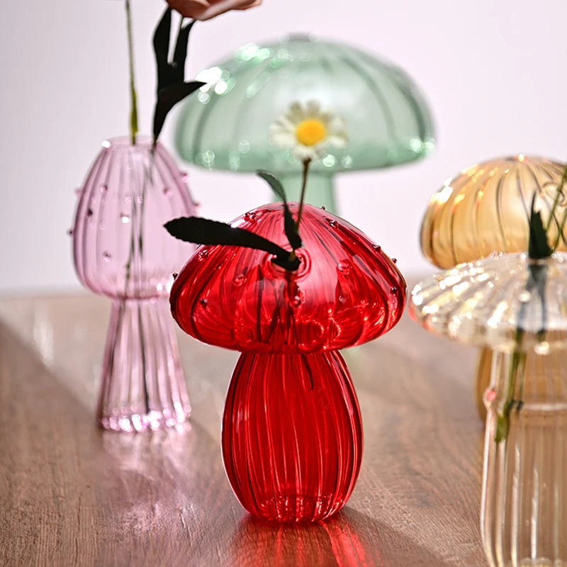 Collection de vases en verre de champignons rouges et roses sur une surface en bois.