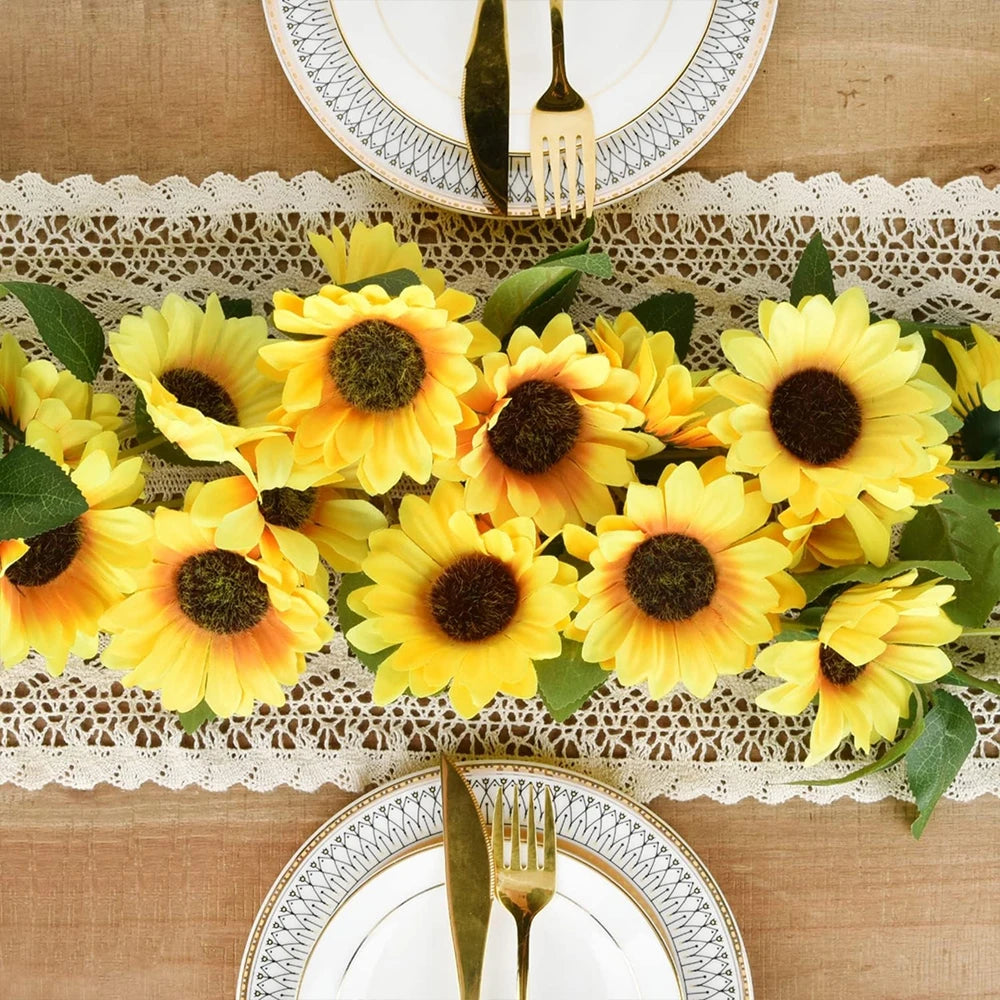 A vibrant yellow silk sunflower vine garland displayed on a wooden surface with decorative plates.