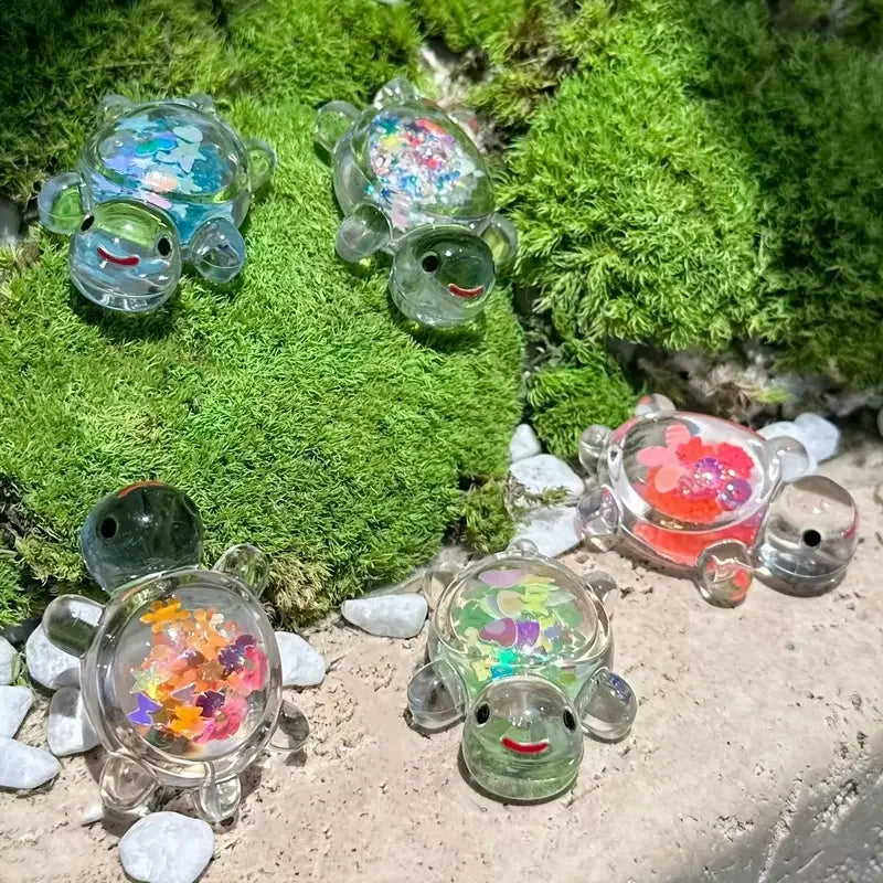 Colección de pequeñas estatuas de tortugas marinas translúcidas de varios colores sobre musgo y guijarros.