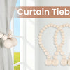 A set of natural wooden bead curtain tiebacks used to hold a light gray curtain open near a window.