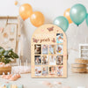 A wooden milestone board featuring photos of a baby from newborn to twelve months, decorated with pink and gold butterflies.