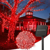 A solar-powered LED string light fixture illuminating a large tree and a house with red lights in an outdoor setting.