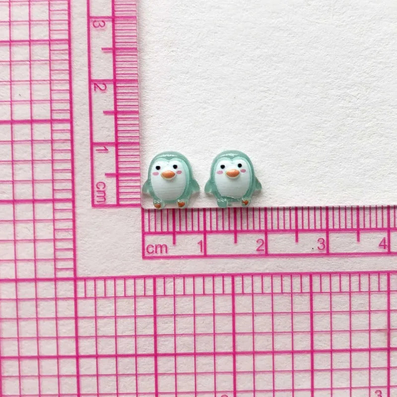 A pair of small, light green resin penguin figurines placed on a pink ruler.